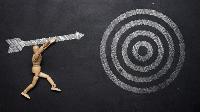 Wooden Mannequin Aiming Large Arrow at Target on Black Chalkboard
