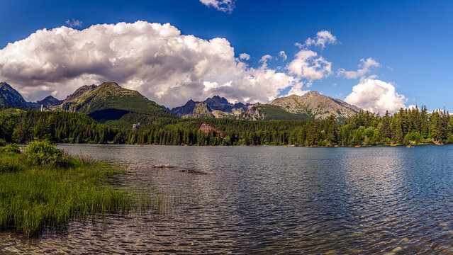 Tranquil Summer Mountain Lake With Forested Shoreline and Dramatic Clouds Over Rugged Peaks