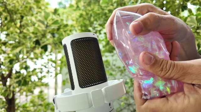 Close up hands squeezing iridescent plastic foil bag near condenser microphone for ASMR crinkling sound triggers concept