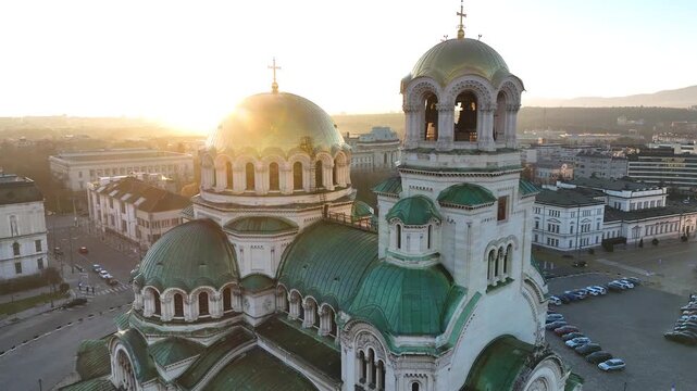 Aerial footage of Alexander Nevsky Cathedral in Sofia, Bulgaria at sunrise, showcasing its iconic golden domes, ornate architecture, surrounding city and Vitosha Mountain.