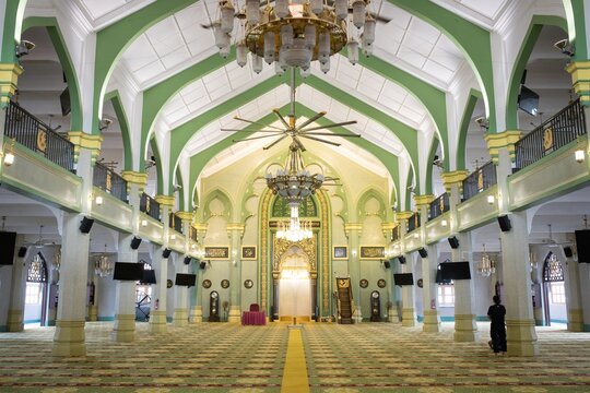 Interior of mosque prayer hall with large chandelier, green arches and prayer mat carpet, Singapore