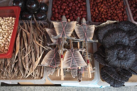 Dried gecko tied to bamboo splints, red jujube fruit, lotus seeds, dried fish, and black mushroom are displayed for sale at a traditional dried goods market stall