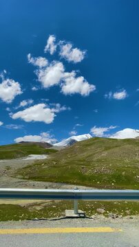 Beautiful high altitude landscape at Khunjerab Pass in Gilgit-Baltistan, northern Pakistan, featuring rolling green terrain, distant snow-covered mountains, and dramatic white clouds.