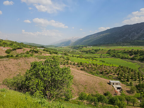 A house rests among orchard rows on a terraced hillside, overlooking a sweeping valley bordered by mountain ridges under a partly cloudy sky
📍 Marivan, Kurdistan, Iran 
