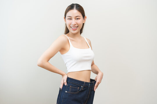 Shape slender, thin waist, slim fit asian young woman, showing body shape her weight loss, happy wearing in big, large or oversize jeans, excess lose by diet and exercise. Healthy lifestyle concept