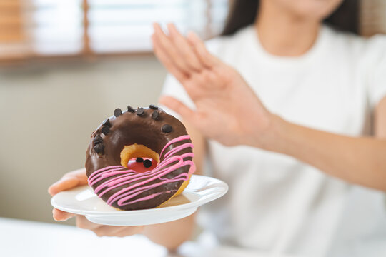 Diet concept, asian young woman hand push out, deny sugar donut, doughnut and sweet taste food on plate, fighting to keep it from getting fat when person bring to me. Healthy nutrition of weight loss.