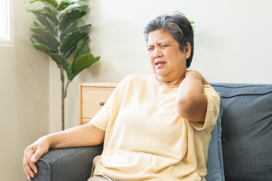 Pain body muscles stiff problem, suffer asian senior woman painful, older hand holding neck ache and aged holding massaging rubbing body, injury hurt,sore sitting on sofa at home. Health care concept.