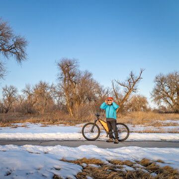 senior cyclist with a mountain bike is taking a rest stop on Poudre River Trail near Greeley, Colorado, in winter scenery