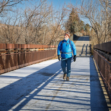 older man with a backpack is walking on a biking trail and footbridge covered by frost, winter morning in Fort Collins, Colorado