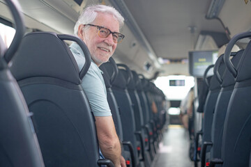 Fototapeta na wymiar Senior adult man with grey hair and beard smiling while looking back from his seat on a public transport bus, enjoying independent travel and comfortable commuting