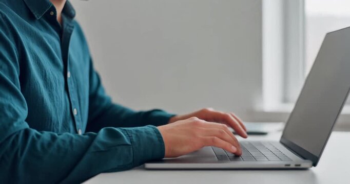 Man wearing teal button shirt typing on laptop computer at workspace