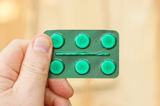 hand holding one plastic green full blister pack of medical pills on brown background