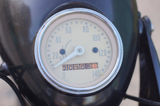 A one old round gray retro speedometer on an old black motorcycle on a street a summer day in the street