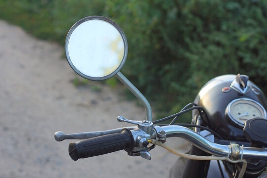 one small old round rearview mirror on the handlebars of an old black retro motorcycle on a daytime summer street