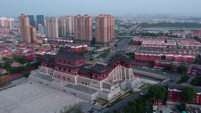 A grand traditional Chinese palace-style building stands in a modern urban area, surrounded by high-rise residential buildings and open plazas.