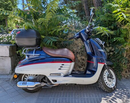Vista lateral de moto scooter Peugeot Django Classic TT 125 con ba&uacute;l trasero, estacionada en Madrid, Espa&ntilde;a, 10 de junio de 2026