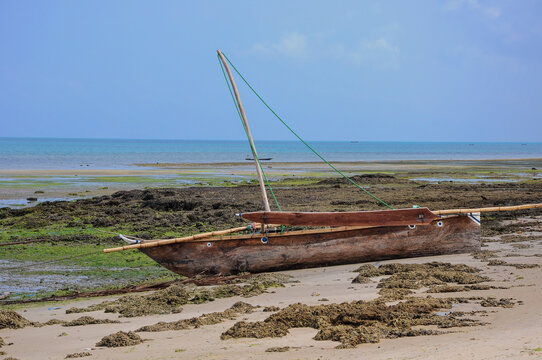 One weathered, wooden homemade boat in sand with water in background in Zanzibar