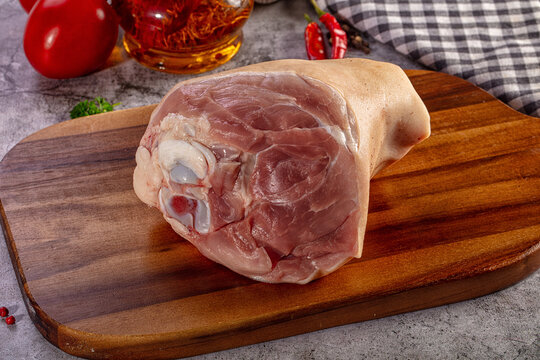 Raw pork knuckle on a wooden cutting board with tomatoes and spices for cooking