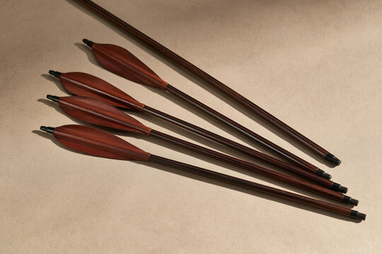 Traditional wooden arrows with dark fletching lie neatly arranged on a textured surface. Ideal for archery and historical weapon themes.
