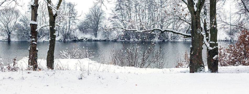 Panoramic view of snow-covered lake surrounded by trees in quiet winter landscape