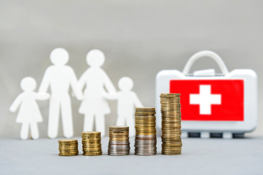 Increasing stacks of coins in front of family figures and a first aid kit represent rising healthcare costs, insurance premiums, medical expenses, and healthcare inflation. Paid medicine