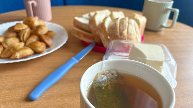Hot tea in ceramic mug with tea bag close-up on blurred food dining table background.