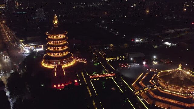Aerial night view of illuminated ancient multi-tiered pagoda and octagonal palace-style buildings, iconic cultural landmarks.
