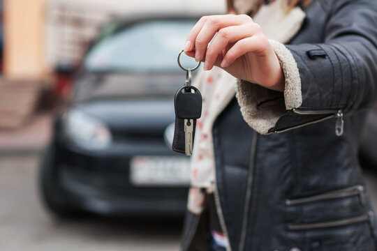 Close-up of a female hand holding modern car keys. Out of focus car background. Ideal for auto insurance, rental services, and vehicle sales concepts.