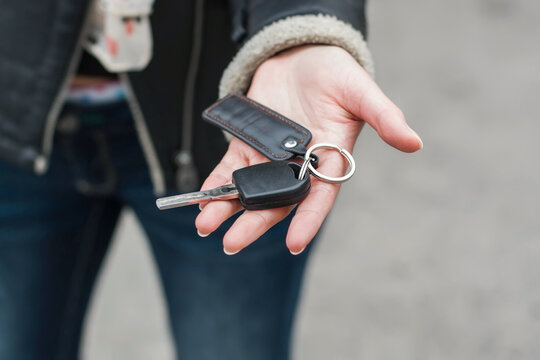 Woman holding black car key with leather fob, closeup of female hand giving or receiving vehicle key for automobile rental, buying, driving or insurance deal.