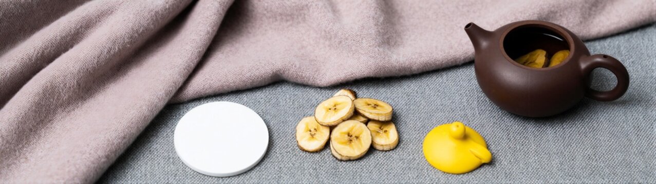 Teapot with banana slices on fabric surface near cloth