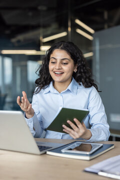Young businesswoman participating in a video conference from her corporate office, actively discussing and taking notes while communicating through her laptop