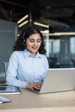 Young woman wearing a headset and light blue shirt working on a laptop, providing customer service and technical support in a modern office environment