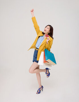 Asian Woman holding credit card and shopping bags celebrating cashless payment consumer confidence retail spending rewards and joyful modern lifestyle.