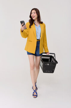Asian Woman using smartphone while carrying shopping basket exploring mobile shopping digital retail deals consumer choice convenient purchasing and modern cashless lifestyle.