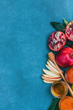 Rosh Hashanah flat lay with pomegranate, sliced apples, and honey on blue background