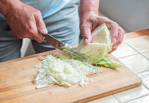 Person's hands chopping fresh green cabbage on a wooden cutting board in a home kitchen, preparing healthy plant based ingredients for a simple, homemade meal