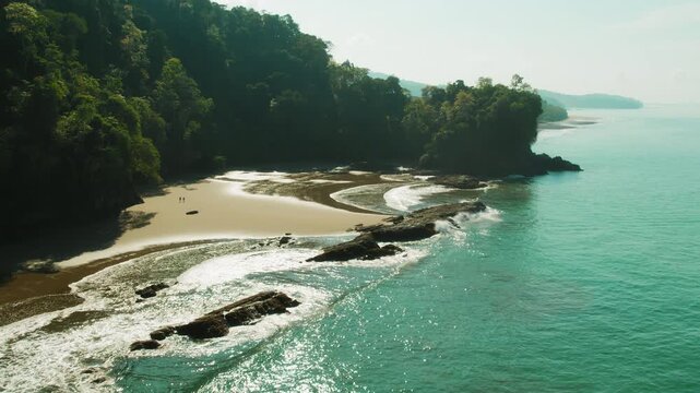 Hidden cove beach below jungle cliffs at low tide on warm tropical sunlight in Costa Rica
