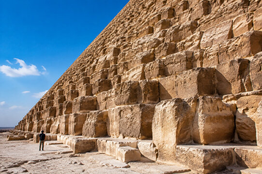 The colossal stone base of an ancient pyramid with a tiny human for scale.