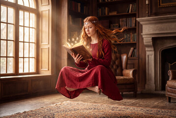 Fototapeta premium A magical redhead woman floating in midair while reading an enchanted glowing book inside a historic library
