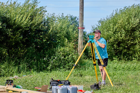 Surveyor operates precision instrument mounted on yellow tripod outdoors, focusing on distant target point.