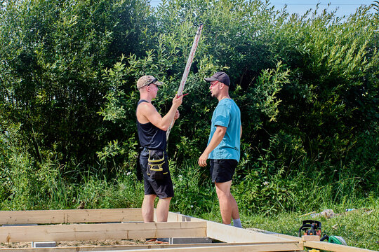 Leveling rod is being held by construction worker while discussing measurements with colleague during outdoor building project.