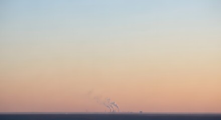 Fototapeta premium Distant industrial smokestacks emitting power plant emissions into a clear soft pastel horizon sky during early morning or sunset