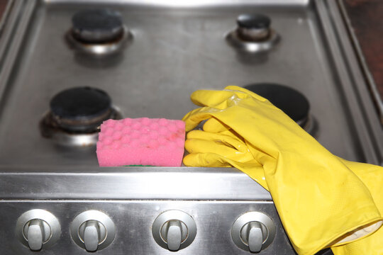 Yellow rubber gloves and pink sponge on a stainless steel gas stove, symbolizing household cleaning, kitchen hygiene, and spring cleaning.