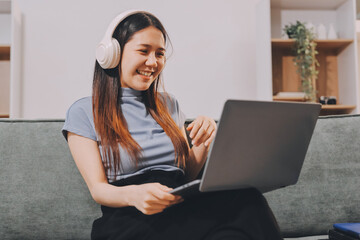 Beautiful young asian woman sitting on sofa and holding joystick playing online video game in living room at house © ARMMY PICCA