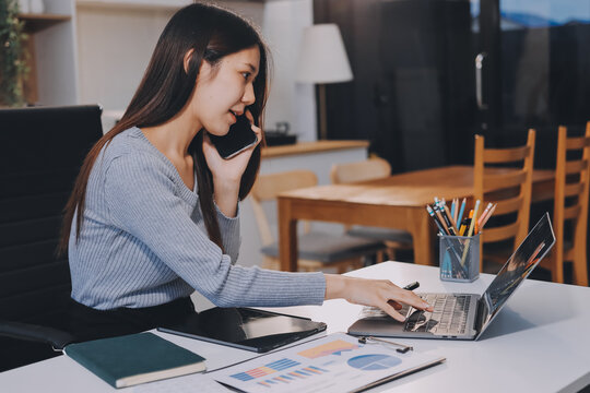 Young Asian woman sits at office desk rubbings her eyes and temples feeling pain. Stress. And exhaustion from long hours working on the computer