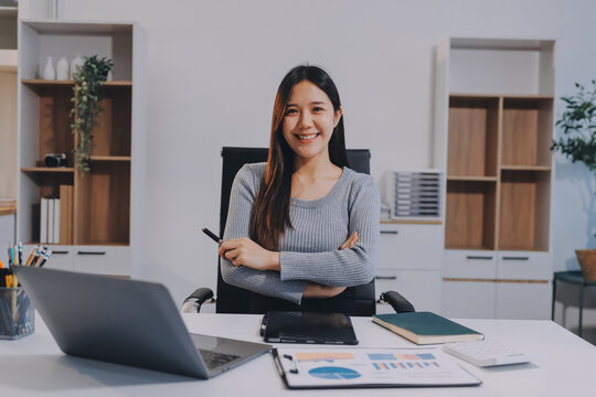 young woman is working on laptop in modern office environment, showcasing focused and productive atmosphere. She is dressed in professional white shirt, with coffee cup and small plant on table,
