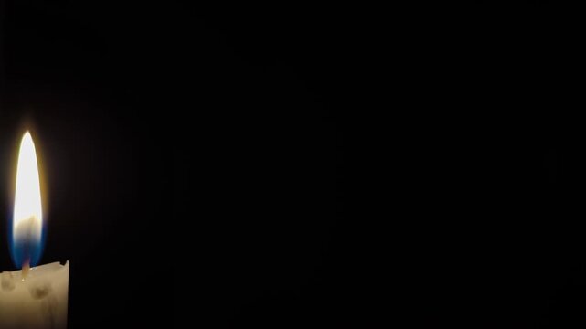 White paraffin candle flame burning. A single white candle burning. White paraffin candle with yellow shades burns on black background. Slow motion. 4K Video