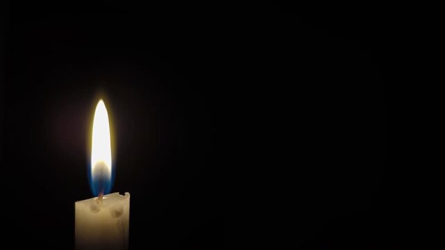 A close up macro shot of a candle flame. White paraffin candle flame burning on black Background. 4K Video