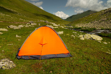 Bright orange camping tent in a grassy mountain valley © yanik88