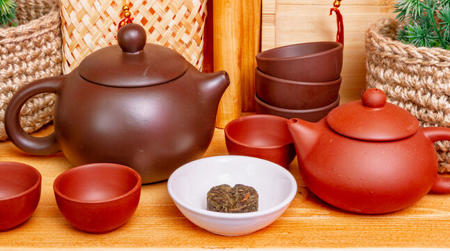 Assorted Yixing zisha clay teapots with red tea cups, white bowl and mini puerh tea cake on wooden table setup